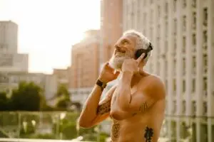 Shirtless mature man listening music with headphones outdoors