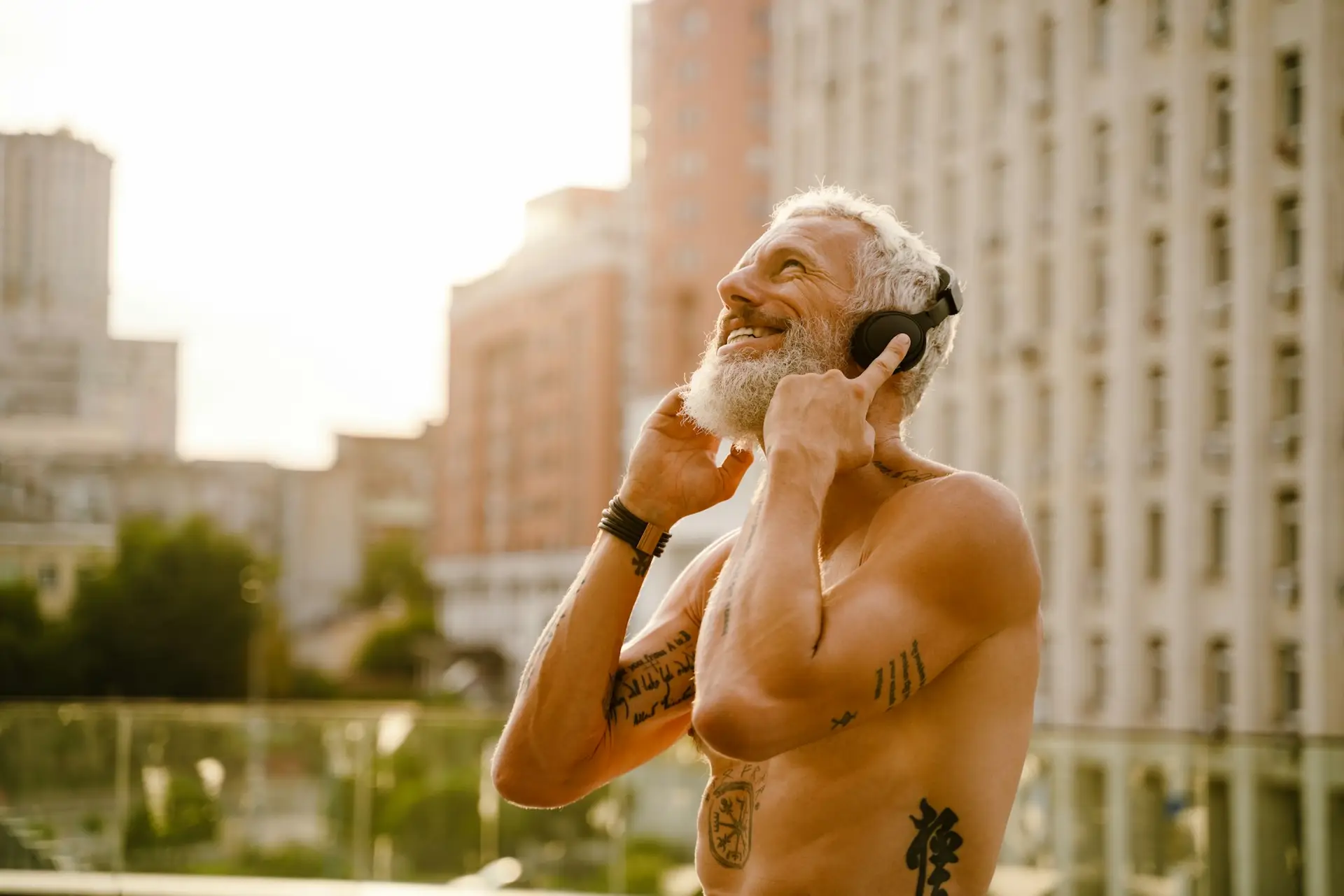 Shirtless mature man listening music with headphones outdoors